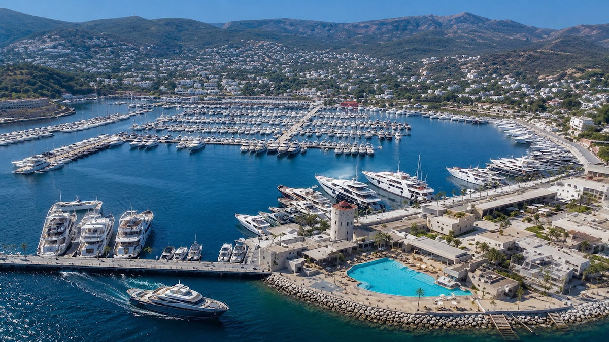 Bodrum Yalıkavak Marina'da lüks yatlar, sahil boyunca uzanan restoranlar, mağazalar ve Ege Denizi manzarası.